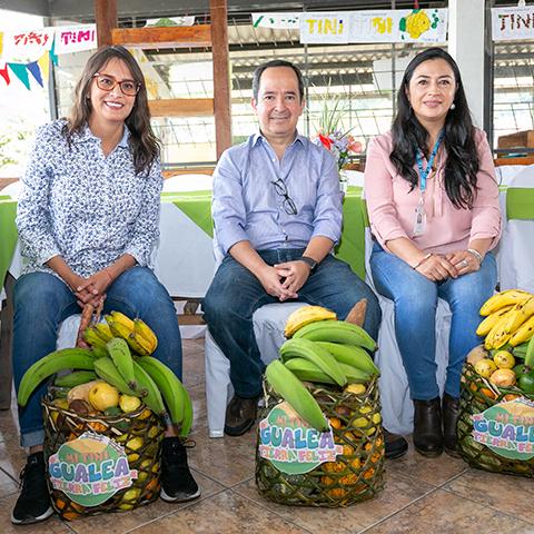 Tres mujeres posan junto a canastas de productos agrícolas durante la actividad.