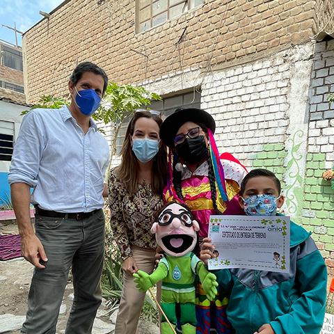 Adultos y profesores posan junto a estudiante junto a la huerta.