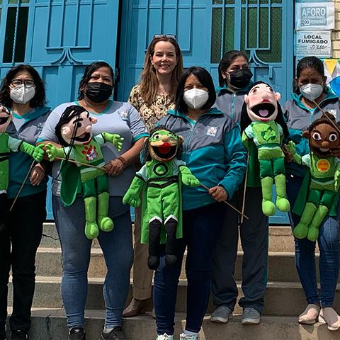 Grupo de estudiantes y adultas sostiene personajes y materiales educativos de la iniciativa.