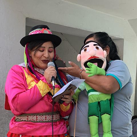 Mujer con traje tradicional interactúa con un personaje durante una actividad para niños.