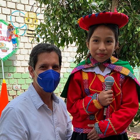 Niña con traje tradicional sostiene un micrófono durante una actividad escolar.